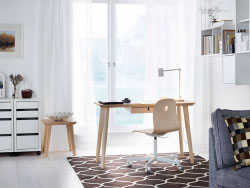 A home office inside living room with a desk in ash veneer and a swivel seat. Combined with white cabinet devices and open wall surface storage space.