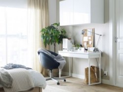 A white table with a black swivel seat on castors and a wall cabinet, inside room.